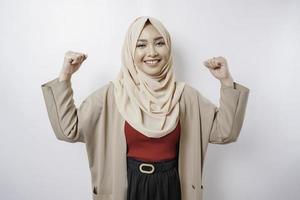femme musulmane asiatique excitée portant un hijab montrant un geste fort en levant les bras et les muscles en souriant fièrement photo