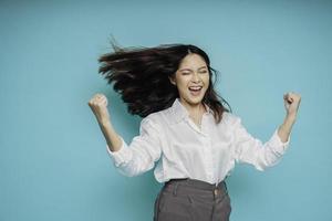 une jeune femme asiatique avec une expression heureuse et réussie portant une chemise blanche isolée par un fond bleu photo