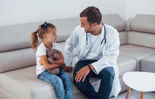 médecin de sexe masculin en uniforme blanc est assis dans la clinique avec une petite fille photo