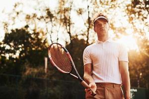 beau soleil. jeune joueur de tennis en vêtements sportifs est sur le terrain à l'extérieur photo