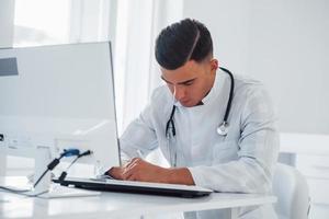 travailler avec des documents. jeune médecin de sexe masculin élégant avec stéthoscope est en clinique pendant la journée photo