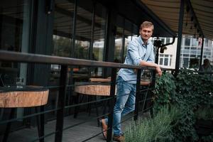 s'appuyant sur les balustrades. vue de face d'un gars en jeans qui se tient dans le café pendant la journée photo