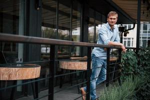 s'appuyant sur les balustrades. vue de face d'un gars en jeans qui se tient dans le café pendant la journée photo