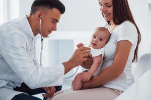 avec l'aide de sa mère. le jeune pédiatre est avec un petit bébé à la clinique pendant la journée photo