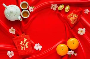 fond de tissu de satin rouge avec service à thé, lingots, mot de sac rouge signifie richesse, oranges et paquets d'enveloppe rouge ou mot ang bao signifie auspice pour le concept du nouvel an chinois. photo