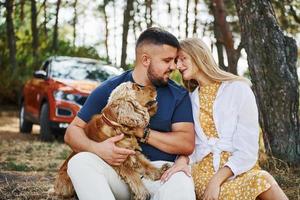 un couple avec un chien passe un week-end à l'extérieur dans la forêt avec une voiture derrière eux photo