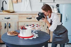 une femme se tient dans la cuisine et prend une photo de ses biscuits et de sa tarte faits maison à l'aide d'un appareil photo