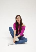 une fille aux cheveux longs dans un pull rose et un jean est assise sur le sol, en studio, sur fond blanc photo