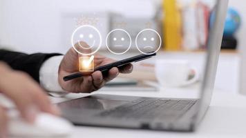 concept d'évaluation du service client. l'utilisation d'un smartphone appuie sur l'émoticône du visage souriant de satisfaction sur l'écran tactile virtuel. photo