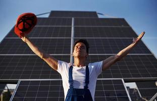 mains levées. travailleur masculin en uniforme bleu à l'extérieur avec des batteries solaires à la journée ensoleillée photo