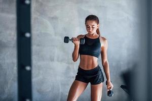 jeune femme fitness est dans la salle de gym avec des haltères dans les mains photo