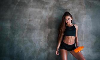 jeune femme de remise en forme avec un corps mince et une bouteille d'eau s'appuie sur le mur photo