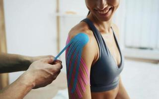 un médecin aide une femme par un traitement de l'épaule avec du ruban kinesio photo