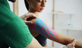 un médecin aide une femme par un traitement de l'épaule avec du ruban kinesio photo