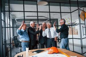 travail bien fait, se donne un high five. une équipe âgée d'architectes d'hommes d'affaires âgés se tient ensemble au bureau photo