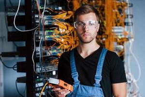 un jeune homme portant des lunettes de protection travaille avec un équipement internet et des fils dans la salle des serveurs photo