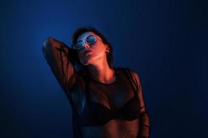 brune chaude à lunettes de soleil posant en studio avec éclairage au néon photo