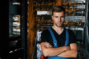 jeune homme en uniforme se dresse contre l'équipement internet dans la salle des serveurs photo