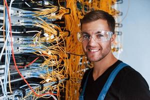 un jeune homme portant des lunettes de protection travaille avec un équipement internet et des fils dans la salle des serveurs photo