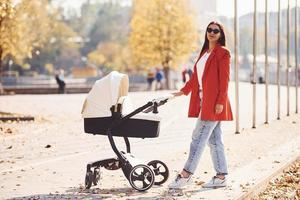 mère en manteau rouge se promener avec son enfant dans le landau dans le parc à l'automne photo