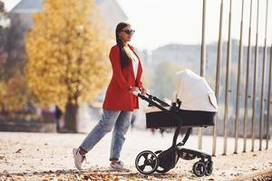 mère en manteau rouge se promener avec son enfant dans le landau dans le parc à l'automne photo