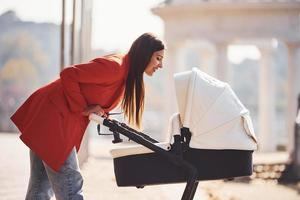 mère en manteau rouge se promener avec son enfant dans le landau dans le parc à l'automne photo