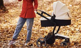 vue rapprochée. mère en manteau rouge se promener avec son enfant dans le landau dans le parc à l'automne photo