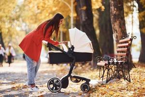 mère en manteau rouge se promener avec son enfant dans le landau dans le parc avec de beaux arbres à l'automne photo