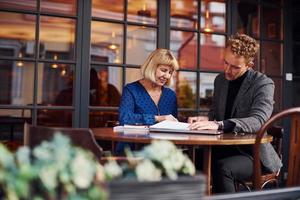 travailler avec des documents. jeune homme en vêtements formels a une conversation d'affaires avec une vieille femme au café photo