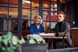 travailler avec des documents. jeune homme en vêtements formels a une conversation d'affaires avec une vieille femme au café photo