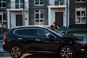 portrait d'un beau jeune homme d'affaires en costume noir et cravate à l'extérieur près d'une voiture moderne dans la ville photo