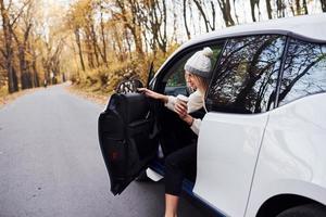 avec une tasse de boisson dans les mains. fille a un voyage d'automne en voiture. automobile neuve et moderne dans la forêt photo