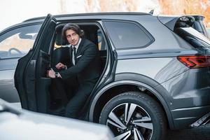 sort de la voiture. jeune homme d'affaires en costume noir et cravate à l'intérieur d'une automobile moderne photo