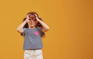 jolie petite fille en tenue décontractée s'amuse en studio sur fond jaune photo