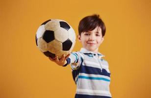 portrait de jeune footballeur avec ballon. se dresse sur fond jaune photo