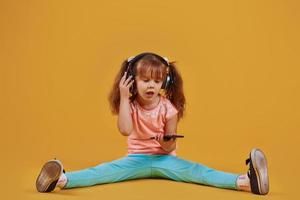 portrait d'une petite fille mignonne dans un casque et avec un téléphone en studio sur fond jaune photo