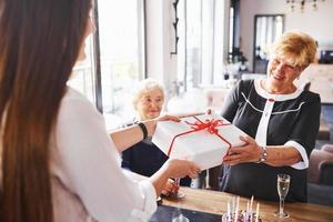 recevoir une boîte cadeau. femme âgée avec famille et amis célébrant un anniversaire à l'intérieur photo