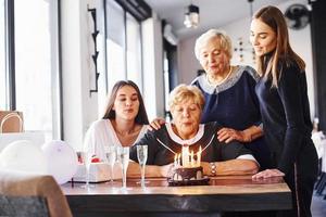 souffler les bougies. femme âgée avec famille et amis célébrant un anniversaire à l'intérieur photo