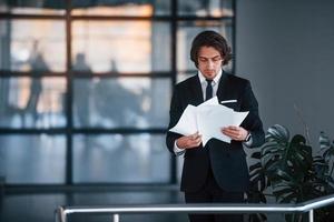 lit des documents. portrait de beau jeune homme d'affaires en costume noir et cravate photo