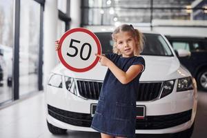 portrait d'une petite fille mignonne qui tient un panneau routier dans les mains dans un salon automobile photo