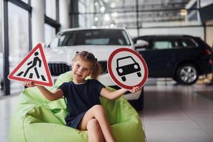 portrait d'une petite fille mignonne qui tient des panneaux routiers dans les mains dans un salon automobile photo