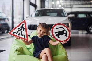 portrait d'une petite fille mignonne qui tient des panneaux routiers dans les mains dans un salon automobile photo