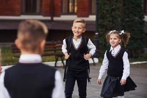 avoir une réunion. groupe d'enfants en uniforme scolaire qui est à l'extérieur ensemble près du bâtiment de l'éducation photo