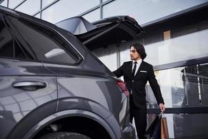 portrait d'un beau jeune homme d'affaires en costume noir et cravate à l'extérieur près d'une voiture moderne photo