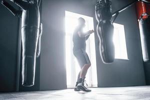 homme en vêtements sportifs s'entraînant à la boxe dans la salle de gym avec des sacs à pousser. illuminé par la lumière photo