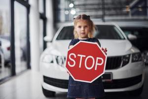 portrait d'une petite fille mignonne qui tient un panneau routier dans les mains dans un salon automobile photo