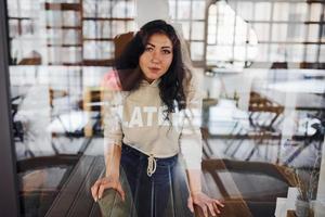 portrait de brune qui se tient à l'intérieur du café. photo à travers le verre