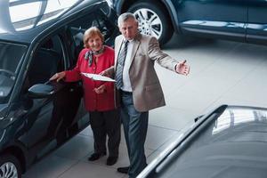 vieil homme en tenue de soirée avec bloc-notes soutenant la femme dans le choix de l'automobile photo