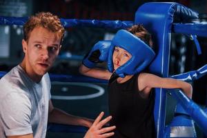 un jeune entraîneur de boxe aide un petit garçon à porter des vêtements de protection sur le ring entre les rounds photo