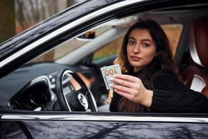 brune assise dans une automobile moderne avec de l'argent dans les mains photo